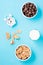 Bowls with cereal flakes and chocolate balls, a glass of milk and an alarm clock on a blue background. Scheduled breakfast