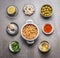 Bowls with Chickpeas salad ingredients: cooked Chickpeas, olives, shrimps, lemon, Paprika powder, herbs,olives oil on gray concret