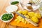 Bowls with chopped dill, scallion, bowl with sour cream, transparent bowl, pieces of baked potatoes, knife on cutting board on