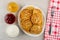 Bowls with lemon jam, strawberry jam, sour cream, dish with cottage cheese pancakes, fork on napkin on wooden table. Top view