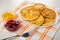 Bowls with lemon jam, strawberry jam, white dish with cottage cheese pancakes, fork on napkin on wooden table