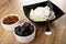 Bowls with raisin and prune, spoon in bowl with grainy cottage cheese and sour cream on wooden table