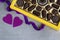 Box of chocolates, two purple decorative hearts and purple ribbon on gray background.