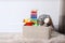 Box with different child toys on floor against white wall.