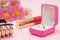 Box with golden ring, lipstick and flowers on a pink background