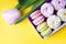 Box with macaroon and marshmallow cakes on a yellow background.