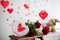 Box in a shape of heart, flowers, red roses and red paper hearts in a Valentine decorated room