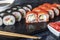 A box of sushi Nigiri, Uramaki California, Philadelphia, on a black stone plate. Sushi menu in a white transport box on a wooden