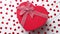 Boxed gift placed on heart shaped red sequins on white wooden table