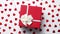 Boxed gift placed on heart shaped red sequins on white wooden table