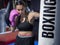 Boxer woman punching a boxing bag with pink gloves in a gym during work out