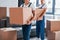 With boxes in hands. Two young movers in blue uniform working indoors in the room