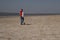 A boy of 10 years old in a white sweatshirt and orange vest plays football on a deserted beach in solitude