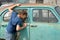 A boy, 11 years old, looks out the window of a rusty car in a dump of abandoned old cars on a sunny summer day