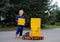 Boy 5-6 years old in a blue overalls uniform stands near a big toy car - a truck with a lot of yellow cardboard boxes