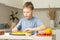 Boy 7-10 in T-shirt cooking pizza in kitchen. Kid arranges ingredients on pizza base