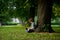 The boy of 8-9 years sits under a big tree, having inclined over the tablet.
