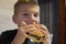 Boy with appetite eats delicious hamburger. child bites off large piece of sandwich