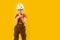 Boy as builder. Child in white helmet, protective glasses wears work jumpsuit and holds drill. Yellow background. Copy space