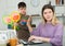 Boy asking mother playing with racquets for tennis, she working at laptop