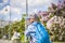 A boy in a baseball cap rides a scooter along a lilac alley .  Against the background of lilac bushes. Interactions. Selective