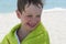 The boy on the beach wrapped in a towel, wet after swimming,