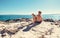 Boy with beagle dog sitting together on rocky sea coast at sunny