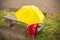 Boy on a bench hidden by a yellow umbrella