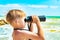 A boy with binoculars looks at the sea against a blue sky