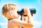 A boy with binoculars looks at the sea against a blue sky