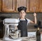 Boy in black chef apron and hat holding metal whisk