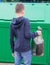A boy in a blue jumper, carries a full bag of garbage to a container to throw it away, rear view