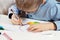 Boy in a blue shirt and glasses sits at a desk and concentrates on doing plastic work with colored paper. The boy is painting