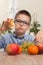 The boy in a blue shirt and glasses sits at the table and holds in his hand an apple which he eats with taste.