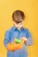 A boy in a blue shirt and orange gloves examines a green washing sponge