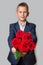 A boy in a blue suit holds a bouquet of red roses. Grey background.