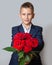 A boy in a blue suit holds a bouquet of red roses. Grey background