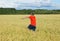 The boy in a bright T-shirt runs along the yellow field where ears of grain grow, the grain against the blue sky, the rear view.