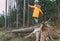 Boy in bright yellow puffer jacket walks in pine forest balancing on the falling tree. People and Nature concept image.