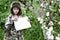 Boy in a camouflage uniform and a hat with earflaps stands in an Apple orchard with a clean white sheet