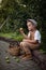 A boy in a cap and beige overalls is harvesting apples. A small farmer holds a pear in his hand