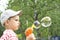 The boy in the cap lets soap bubbles in the summer against the background of green birches