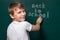 A boy of Caucasian appearance writes back to school on the chalkboard. Looking at the camera. Beginning of the school year