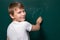 A boy of Caucasian appearance writes a question mark on the chalkboard. Looking into the camera. Smile. Easy solution to the