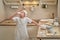 A boy in chef clothes drinks milk from a glass while cooking an apple pie in the kitchen