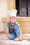 A boy in chef`s hats near the fireplace sitting on the kitchen floor soiled with flour, playing with food, making mess