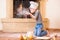 A boy in chef`s hats near the fireplace sitting on the kitchen floor soiled with flour, playing with food, making mess