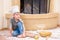 A boy in chef`s hats near the fireplace sitting on the kitchen floor soiled with flour, playing with food, making mess