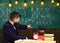 Boy, child in graduate cap looks at scribbles on chalkboard while teacher explains. Teacher with beard, father teaches