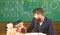 Boy, child in graduate cap looks at scribbles on chalkboard while teacher explains. Teacher with beard, father teaches